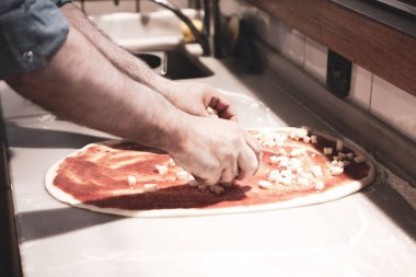 Pizza şefi ticari bir mutfakta sosu tabana koydu.