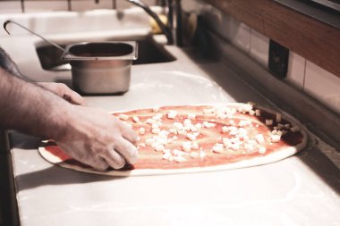 Pizza şefi ticari bir mutfakta sosu tabana koydu.