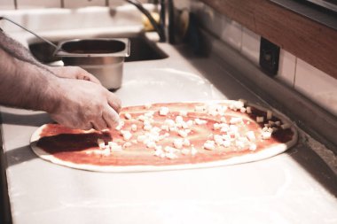 Pizza şefi ticari bir mutfakta sosu tabana koydu.
