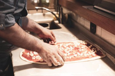 Pizza şefi ticari bir mutfakta sosu tabana koydu.