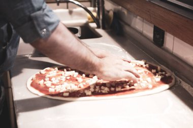 Pizza şefi ticari bir mutfakta sosu tabana koydu.