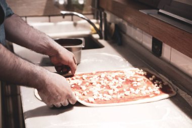 Pizza şefi ticari bir mutfakta sosu tabana koydu.