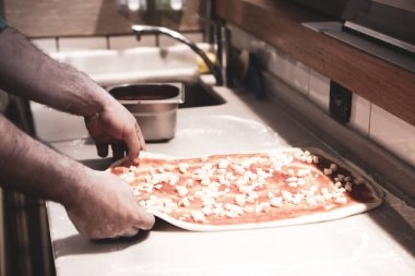 Pizza şefi ticari bir mutfakta sosu tabana koydu.