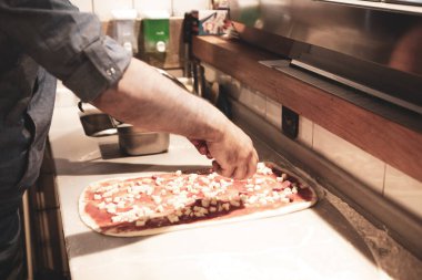 Pizza şefi ticari bir mutfakta sosu tabana koydu.