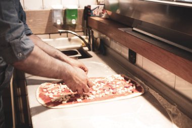 Pizza şefi ticari bir mutfakta sosu tabana koydu.