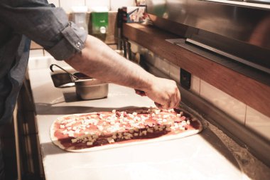 Pizza şefi ticari bir mutfakta sosu tabana koydu.
