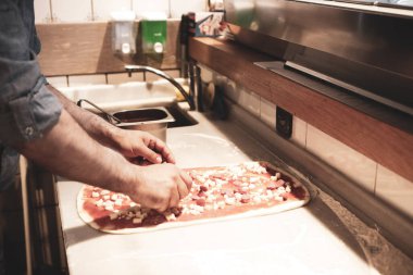 Pizza şefi ticari bir mutfakta sosu tabana koydu.