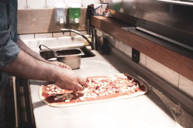 Pizza şefi ticari bir mutfakta sosu tabana koydu.