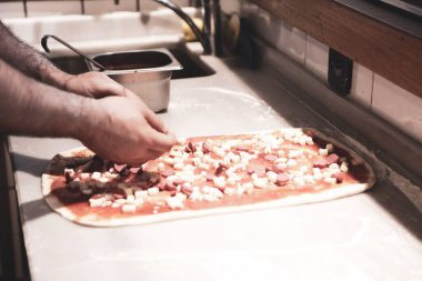 Pizza şefi ticari bir mutfakta sosu tabana koydu.