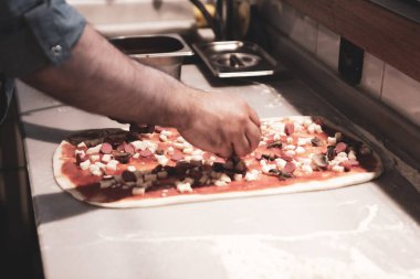 Pizza şefi ticari bir mutfakta sosu tabana koydu.