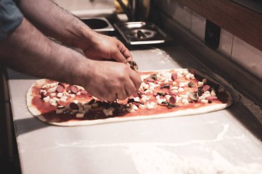 Pizza şefi ticari bir mutfakta sosu tabana koydu.