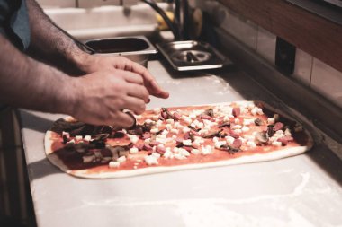Pizza şefi ticari bir mutfakta sosu tabana koydu.