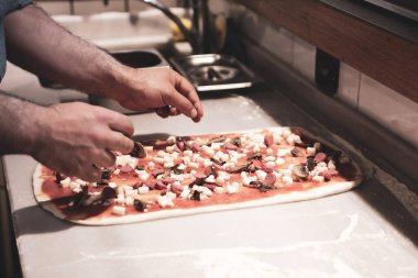 Pizza şefi ticari bir mutfakta sosu tabana koydu.