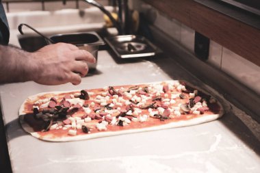 Pizza şefi ticari bir mutfakta sosu tabana koydu.