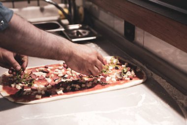 Pizza şefi ticari bir mutfakta sosu tabana koydu.