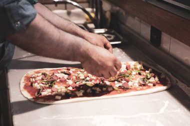 Pizza şefi ticari bir mutfakta sosu tabana koydu.