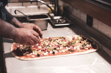 Pizza şefi ticari bir mutfakta sosu tabana koydu.