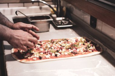 Pizza şefi ticari bir mutfakta sosu tabana koydu.