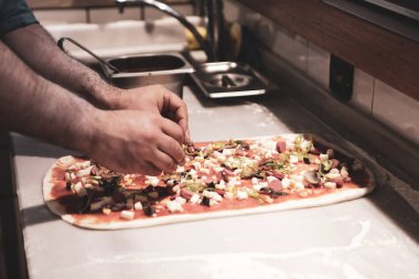 Pizza şefi ticari bir mutfakta sosu tabana koydu.