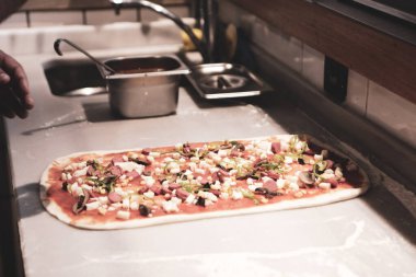 Pizza şefi ticari bir mutfakta sosu tabana koydu.