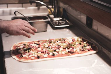 Pizza şefi ticari bir mutfakta sosu tabana koydu.