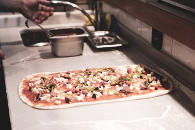 Pizza şefi ticari bir mutfakta sosu tabana koydu.