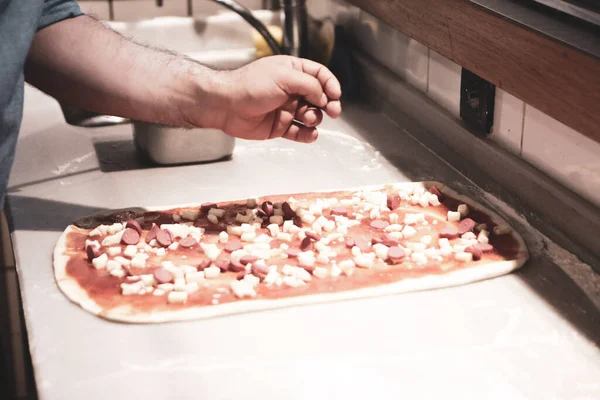 Pizza şefi ticari bir mutfakta sosu tabana koydu.