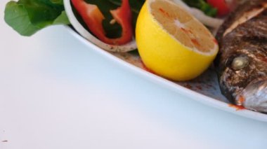 Kızarmış deniz çerezi (cupra) beyaz tabakta soğan, bahçe roketi ve limon dilimli balık.