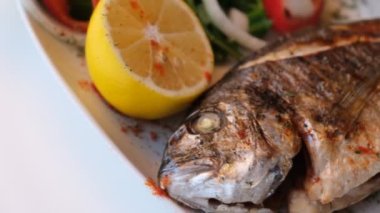 Kızarmış deniz çerezi (cupra) beyaz tabakta soğan, bahçe roketi ve limon dilimli balık.