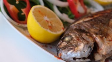 Kızarmış deniz çerezi (cupra) beyaz tabakta soğan, bahçe roketi ve limon dilimli balık.