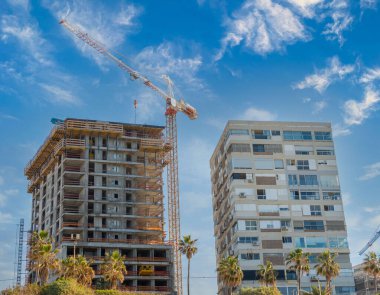 Bat Yam, İsrail, 7 Ocak 2022. Çok katlı bir binanın inşaatı, beyaz bulutlu mavi gökyüzüne karşı eski bir iskan binasının yanında.