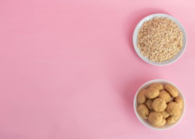 Düz yulaf ezmesi, pembe arka planda beyaz bir tabakta yulaf ezmesi kurabiyesi, üst manzara, sağlıklı beslenme konsepti ve mısır gevreği veya kurabiye yapmak. Metni sola yerleştir