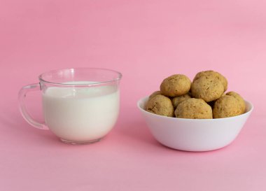 Beyaz tabakta yulaflı kurabiyeler, pembe arka planda şeffaf cam bir manzarada beyaz süt. Yüksek kaliteli fotoğraf.