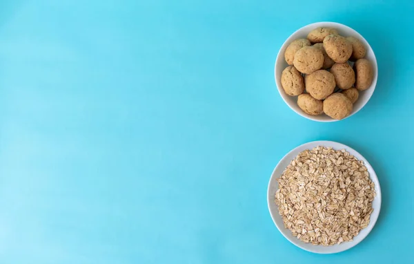 Flatlay oatmeal, oatmeal cookies on a white plate on a blue background, top view, healthy eating concept, and making cereal or cookies. A place for text on the left. High-quality photo