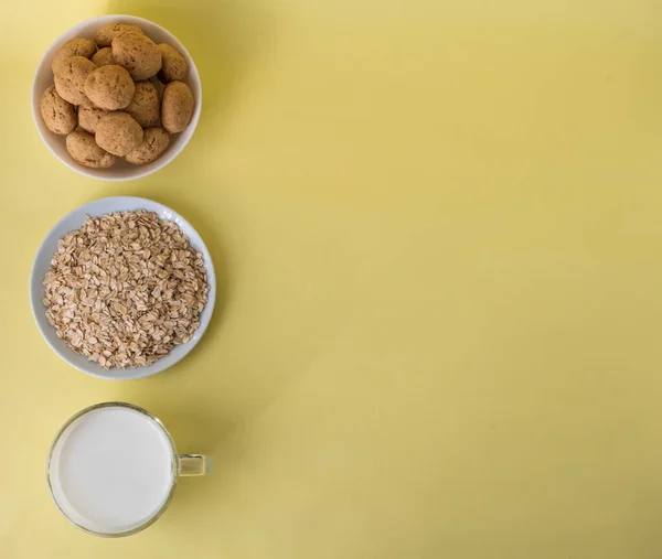 Flat lay white milk, oatmeal, and oatmeal cookies on a white plate on a yellow background, top view, the concept of healthy eating and preparing a healthy breakfast. Space for text on the right. High