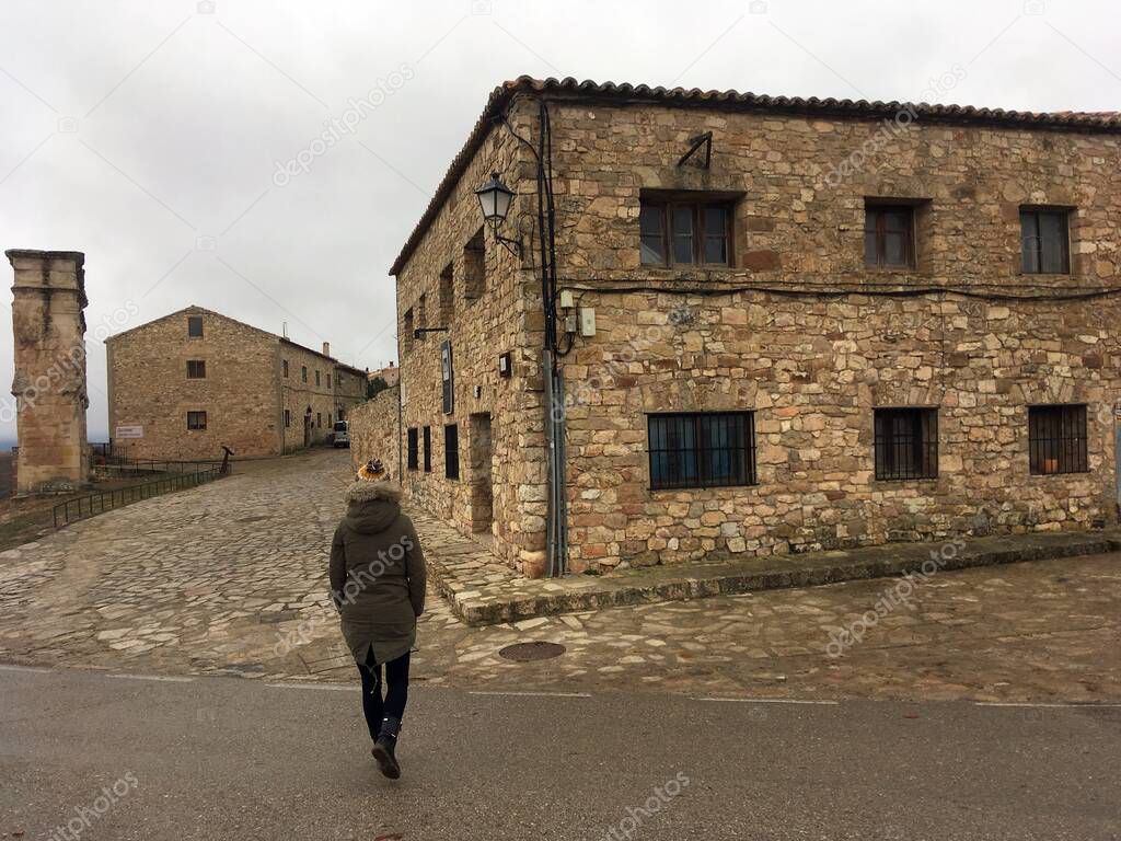 Streets of the historical town of Medinaceli in Soria, Spain. Girl in a coat and a woolen hat walking through the square with her back to the camera.