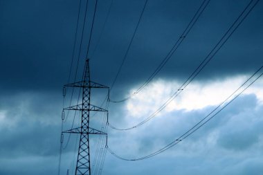 Elektrik iletimi için yüksek voltaj kulesi. Fotoğraf, bulutlu bir günde gün batımında çekildi. Siluetin karanlık gökyüzüne karşı durduğu yerde..