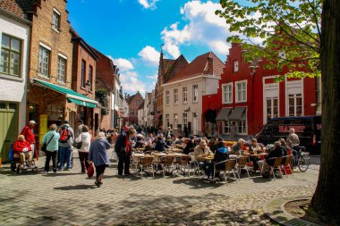 Bruges, Belçika; 04 28 2016. Bruges 'deki Walplein Meydanı' ndaki restoranlarda turistler ve yerliler. Geleneksel evlerin cepheleri arasındaki bir restoranın resimli fotoğrafı..