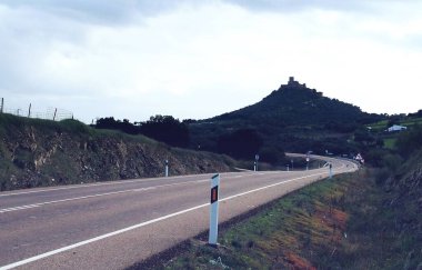 Arkasında Alconchel 'deki Miraflores kalesi olan eski 107 yolu. Bulutlu bir günde şatonun tepenin üstünde olduğu kırsal asfalt yol. Alconchel, Badajoz, İspanya.