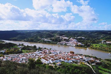 Sanlucar de Guadiana İspanyol kasabası ve Guadiana Nehri kıyısındaki Portekiz Alcoutim. İber Yarımadası 'nın güneybatısında ve tepelerle çevrili iki küçük beyaz ev..