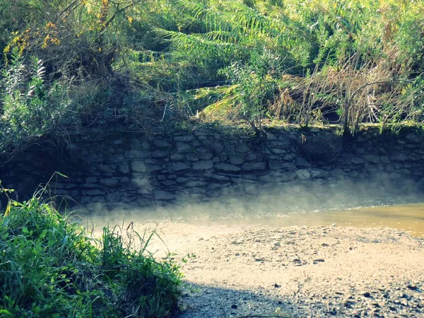 Remains of the water retaining wall of a water mill in Sanlucar de Guadiana, Andalusia, Spain. Water mist next to the ruins of the wall on the banks of a tributary of the Guadiana river.