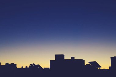 Silhouette of the top of a modern building in Madrid, Spain. Silhouette of the solar panels and chimneys located on the roof with the first rays of the sun in a yellow and blue sky.