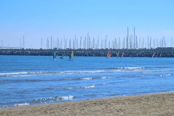 Windsurfing and paddle surfing at Malvarrosa beach in Valencia, Spain. Active people practicing water sports with the breakwater of the port of Valencia in the background.