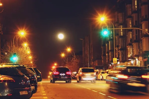 Cars circulating along Monasterio de Silos avenue in Madrid, Spain. Urban scene at night with moving and parked vehicles between the buildings of a residential neighborhood.