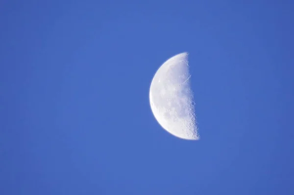 The third quarter moon in a clear blue sky. The brightness of the moon contrasts with the blue of the day.