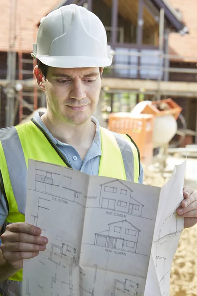 Trabajador de la construcción en el sitio de construcción mirando los planes de la casa — Foto de Stock