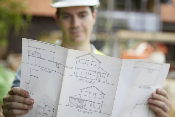 Stavební dělník na stavbě při pohledu na dům plány — Stock fotografie