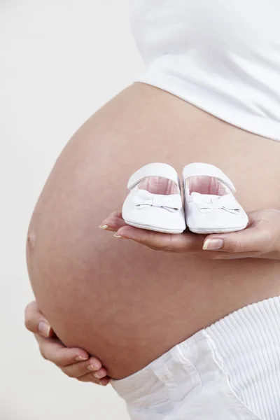 Gros plan de femme enceinte tenant des chaussures de bébé — Photo