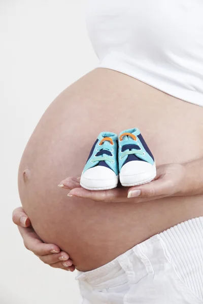 Заткнуть рот беременной женщине, держа в руках детскую обувь — стоковое фото