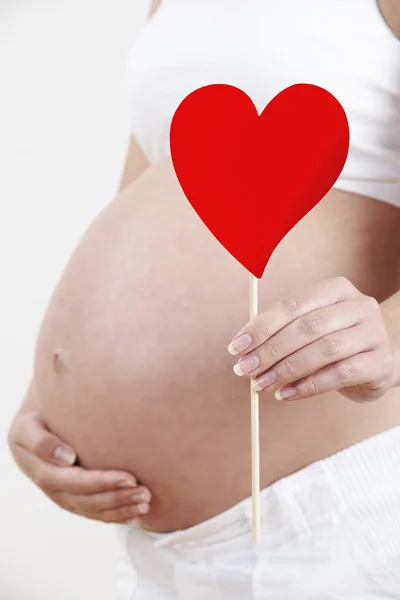 Закрыть беременную женщину, держащую сердце на стежке — стоковое фото